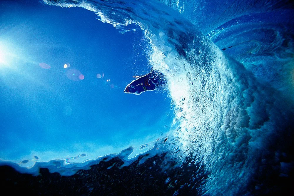 Surf photography print of Pancho Sullivan surfing Cloudbreak, Fiji, captured underwater from beneath the wave with sunrays filtering through the blue ocean.