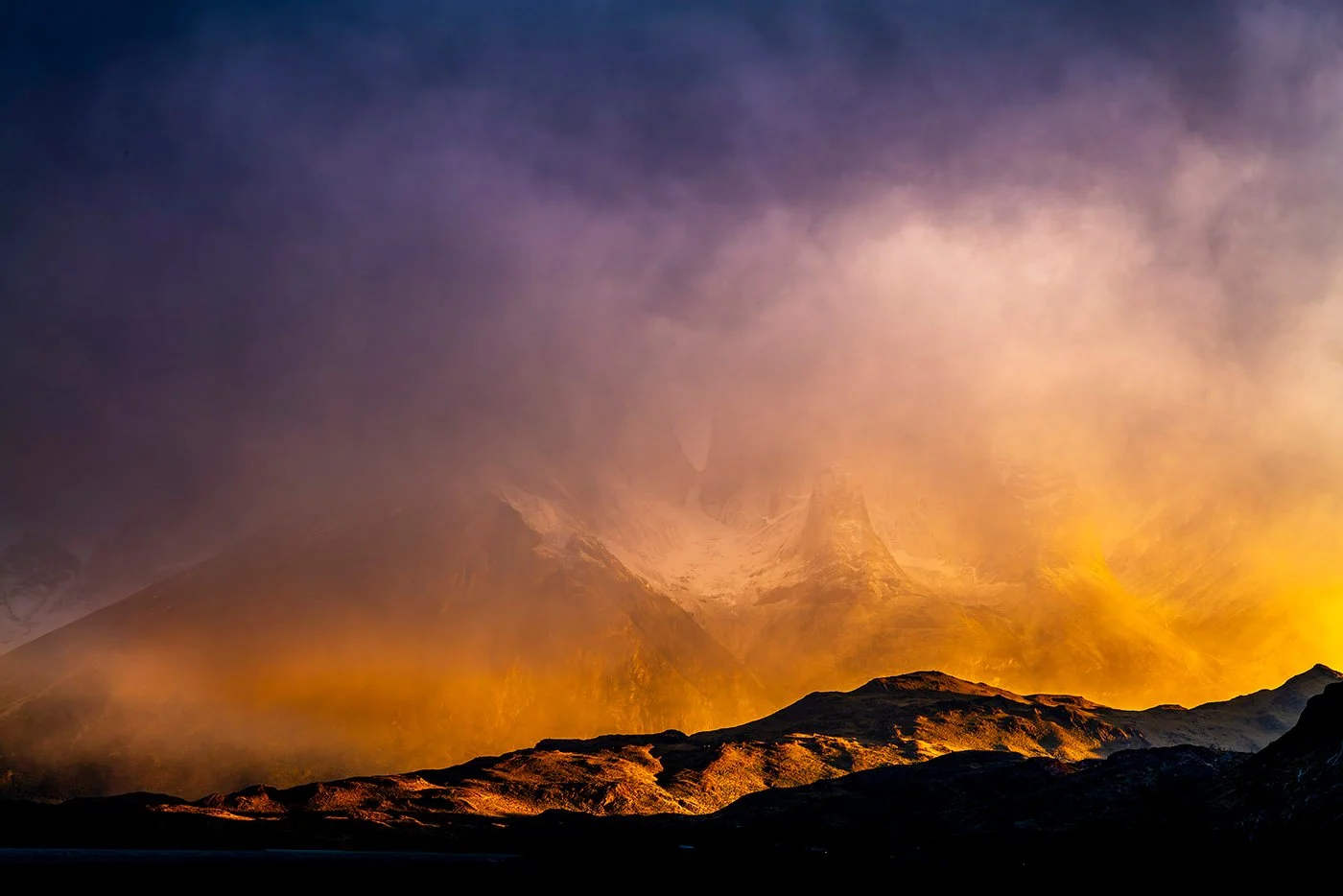 Sunrise light on mountain ridges and a mist-filled valley beneath storm clouds at Torres del Paine, Patagonia.