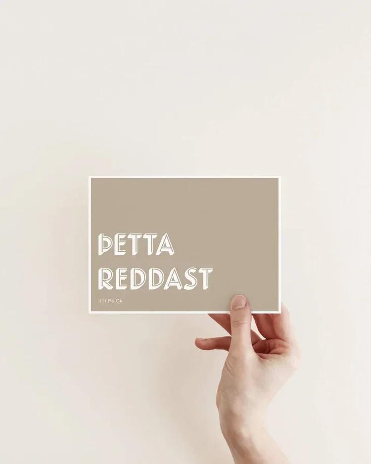 Hand holding a minimalist postcard with the Icelandic phrase “Þetta reddast” in white typography on a warm neutral background, Scandinavian style.