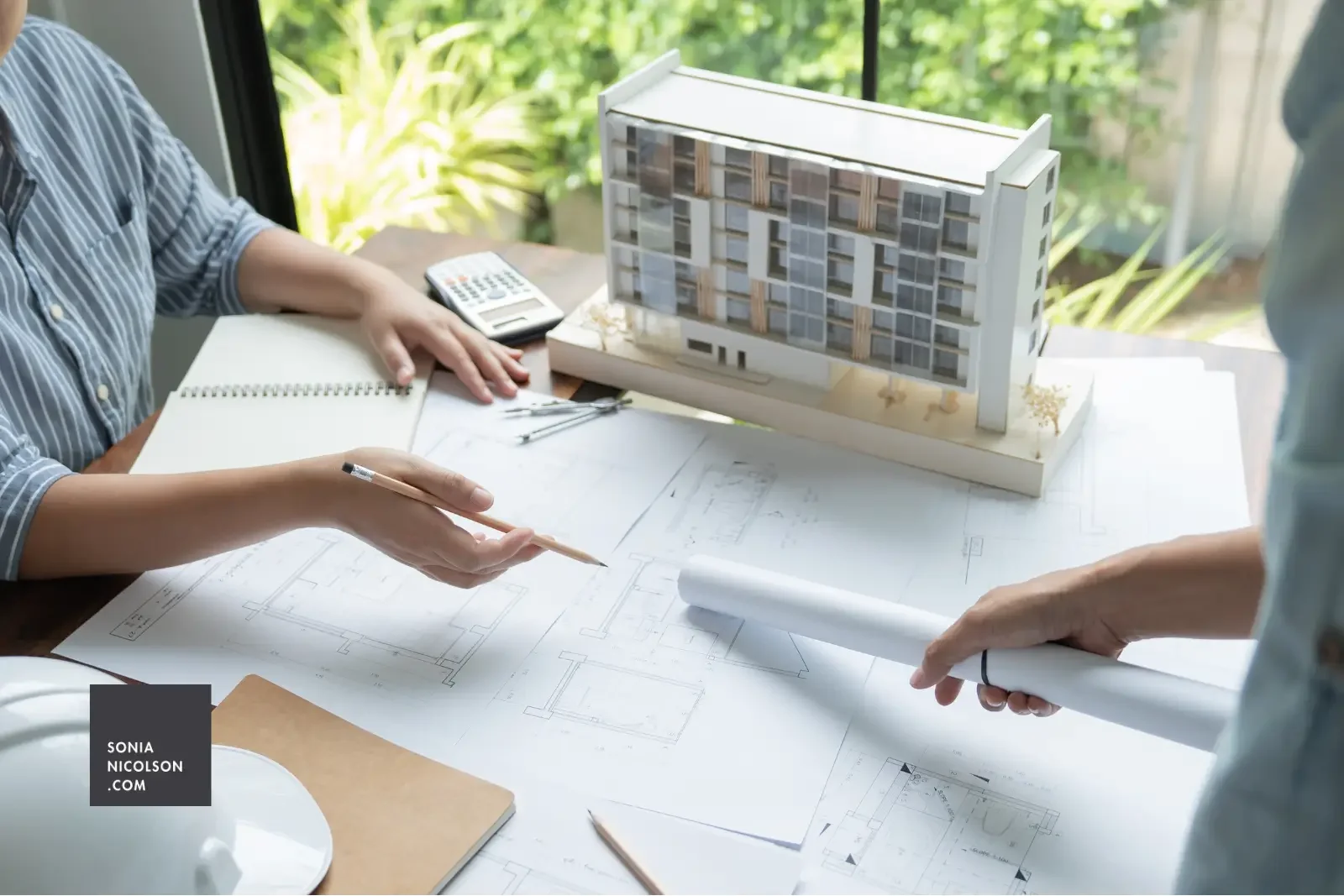 Architecture students reviewing technical drawings and a building scale model during a design project