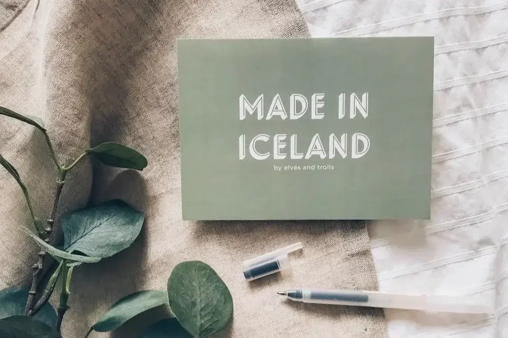 Made in Iceland postcard on natural fabric with pen and leaves – styled flat lay image representing Sonia Nicolson’s Icelandic art and wholesale prints