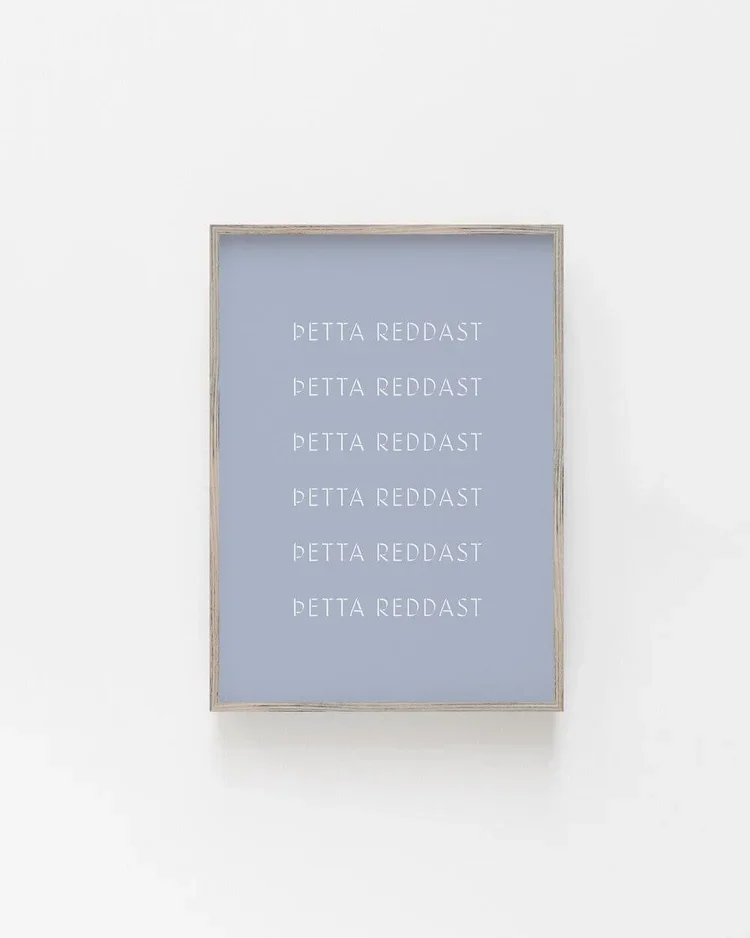 Framed minimalist Icelandic typography wall art featuring the phrase “Þetta reddast” in white text on a soft blue background in a Scandinavian interior.