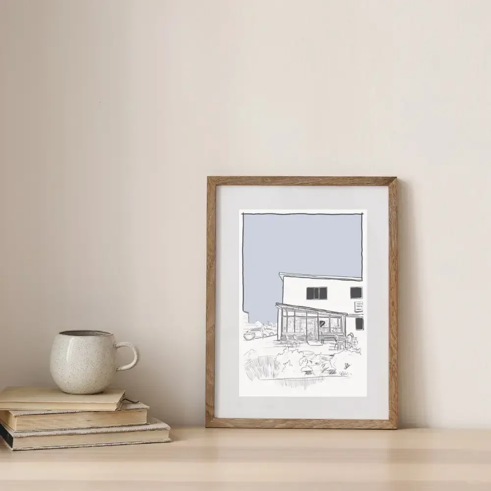 Framed digital architectural line drawing of Kaffihús Vesturbæjar in Reykjavík, Iceland, displayed on a styled shelf with books and a ceramic mug.