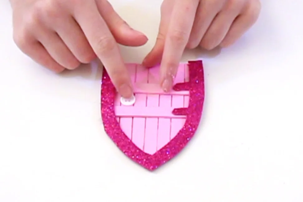 Step 5 Draw around the fairy door on the back of a sheet of glitter foam, then draw an archway wide enough to cover the edges of the sticks. Remember to leave two shapes on the left hand sides for the hinges! Then stick a white button onto the lolly sticks - this will be the door knob.