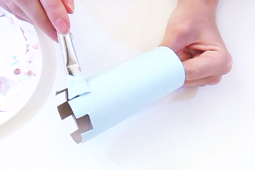 Step 1 Cut squares out of the top of the two toilet rolls to form the top of the castle. Then mix up a shade of light blue (or any colour you want!) and paint them both. Trim the kitchen roll so that it is just taller than the toilet rolls, and paint this the same colour. Also paint the cocktail stick with this paint. Leave to dry. 