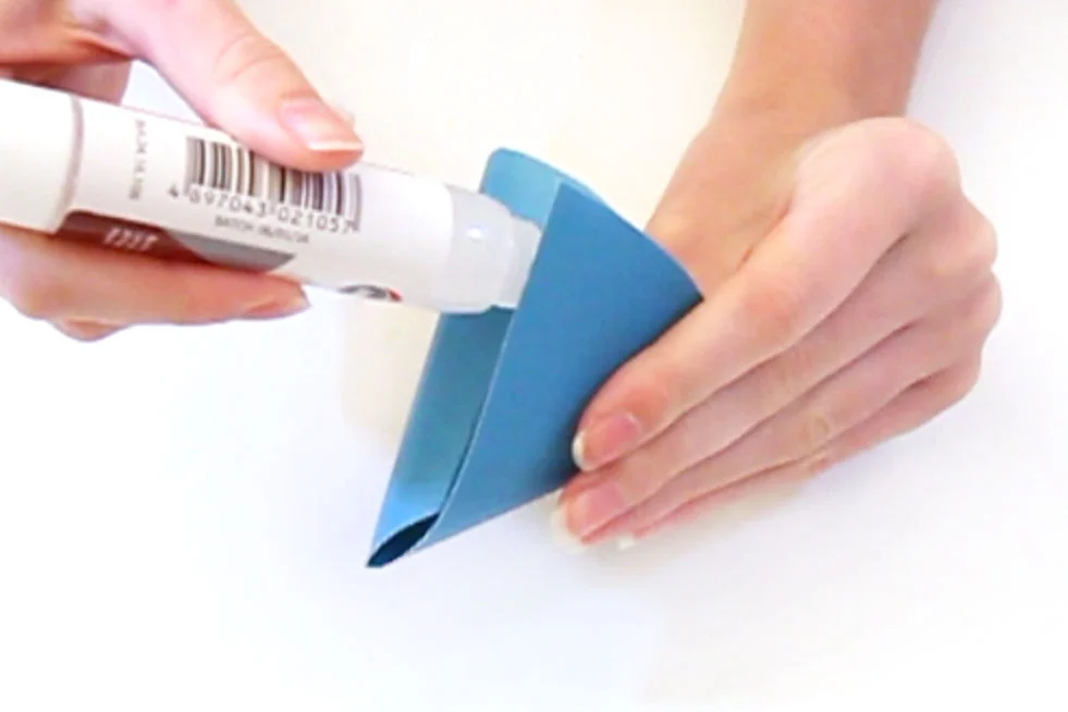 Step 3 Cut a semi circle shape out of the blue paper and make it into a cone shape. Glue down the edges so that the shape holds.