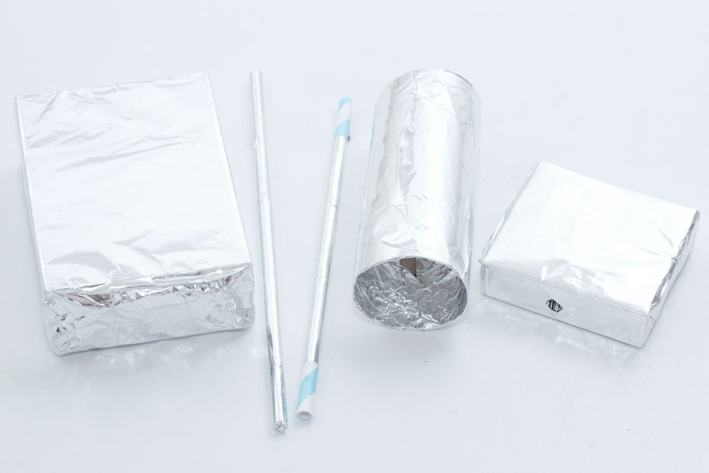 Step 2 Cover the boxes, straws and toilet roll tube in tin foil, gluing and taping where necessary. Once you have covered the boxes, carefully push through the foil where the holes are as you can see in the small box in the photo above.