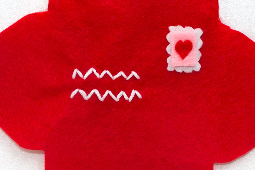Step 2 Make a pretty stamp out of the felt and glue onto the red envelope shape. You can stitch it on if you want to, mine was so tiny I thought it would be to fiddly! Then using the white embroidery thread, stitch a zig zag pattern to mimic where the address would be on the envelope. If you're really good with a needle then you could try stitching actual words on to it!