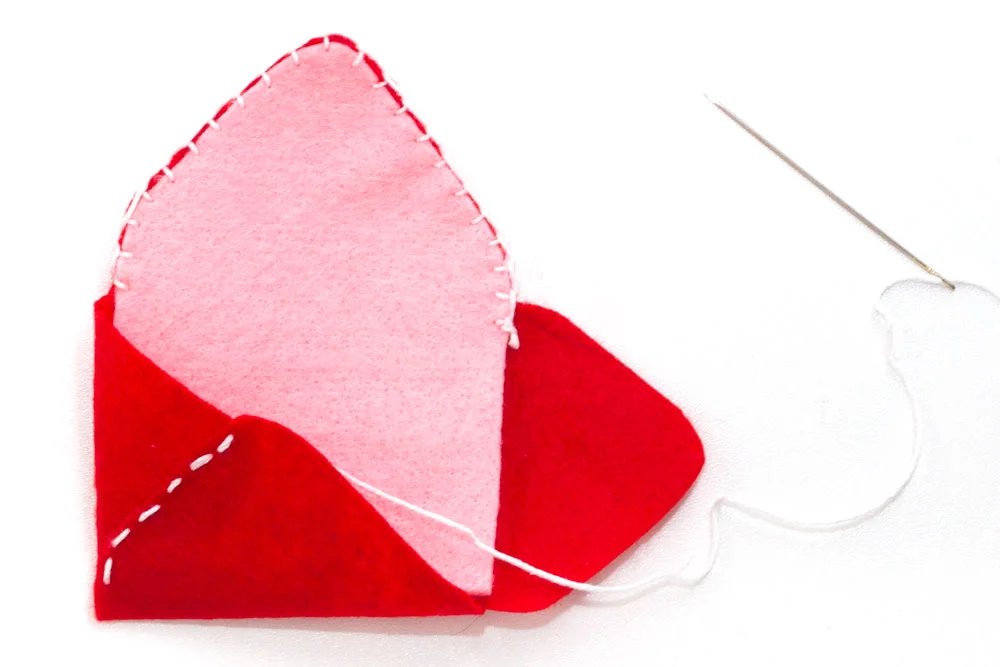 Step 4 Fold the left hand side triangle in towards the middle of the envelope, and fold up the bottom triangle over the top and pin them together. Stitch these two together making sure you don't accidentally sew through the pink felt or the front of the envelope! Repeat this with the other side.