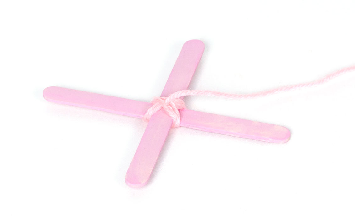 Step 1 Paint two lolly sticks light pink and leave to dry. Add another coat of paint if necessary. Once the paint is dry, add a small strip of double sided tape in the middle of one lolly stick, then stick the other stick on top to create a cross shape. Then wrap some light pink wool around the cross to hold the lolly sticks in place. Thread the end of the pink wool up through the middle and pull tight.