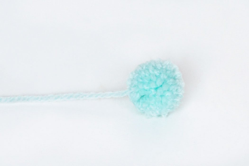 Step 2 Use these instructions to make 8 mini pom poms, 4 light pink and 4 light blue. Leave one end of the wool used to tie the pom pom together long as shown in the picture above.