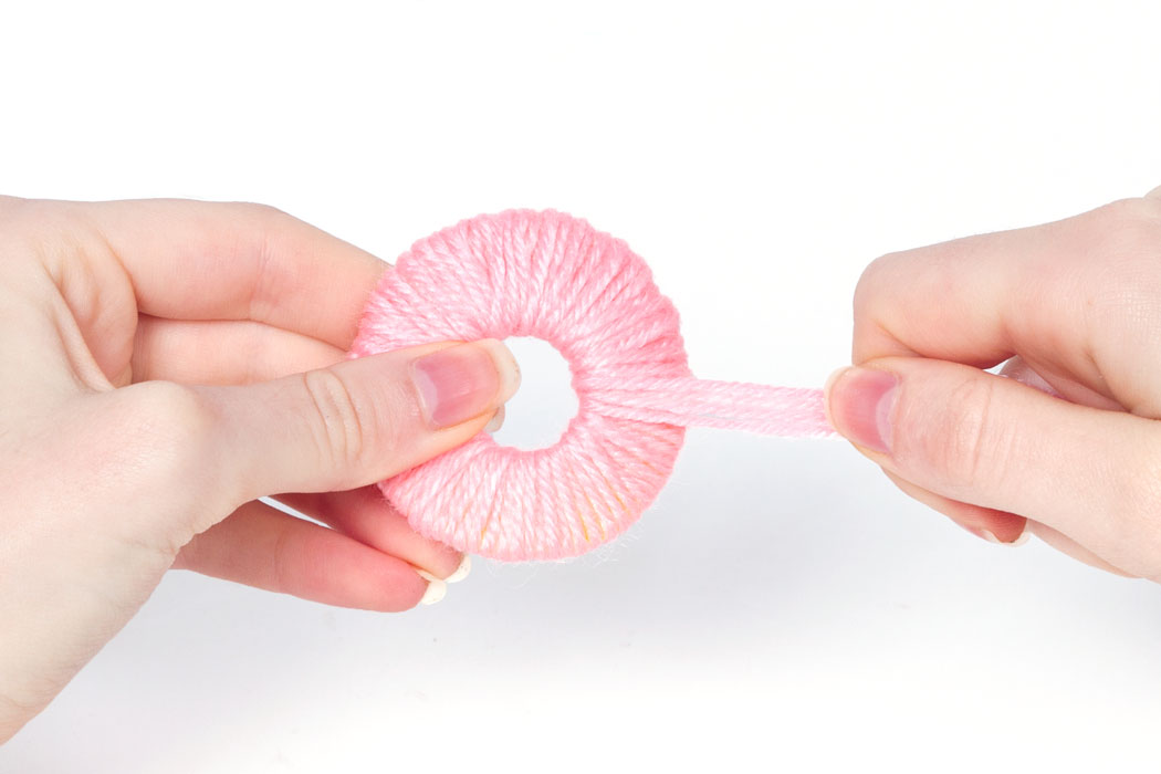 Step 2 Cut a long piece of wool and fold it in half, and then fold it in half again - this is just to make the process of making the pom pom quicker. Start wrapping your wool around the card circle. Do this until the circle in the middle becomes to small to add any more wool.