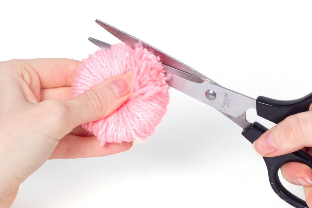 Step 3 Hold the pom pom tightly and start to cut the wool around the edge. Cut the wool the whole way around the circle. Once this is done the wool will be loose so try not to let go of it.