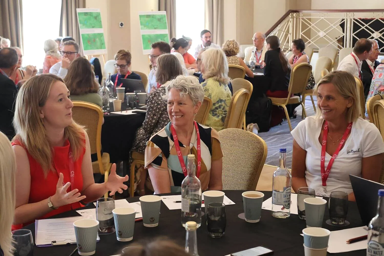 Group of women sitting around a conference table, engaged in discussion, with name tags and conference materials, in a well-lit room.