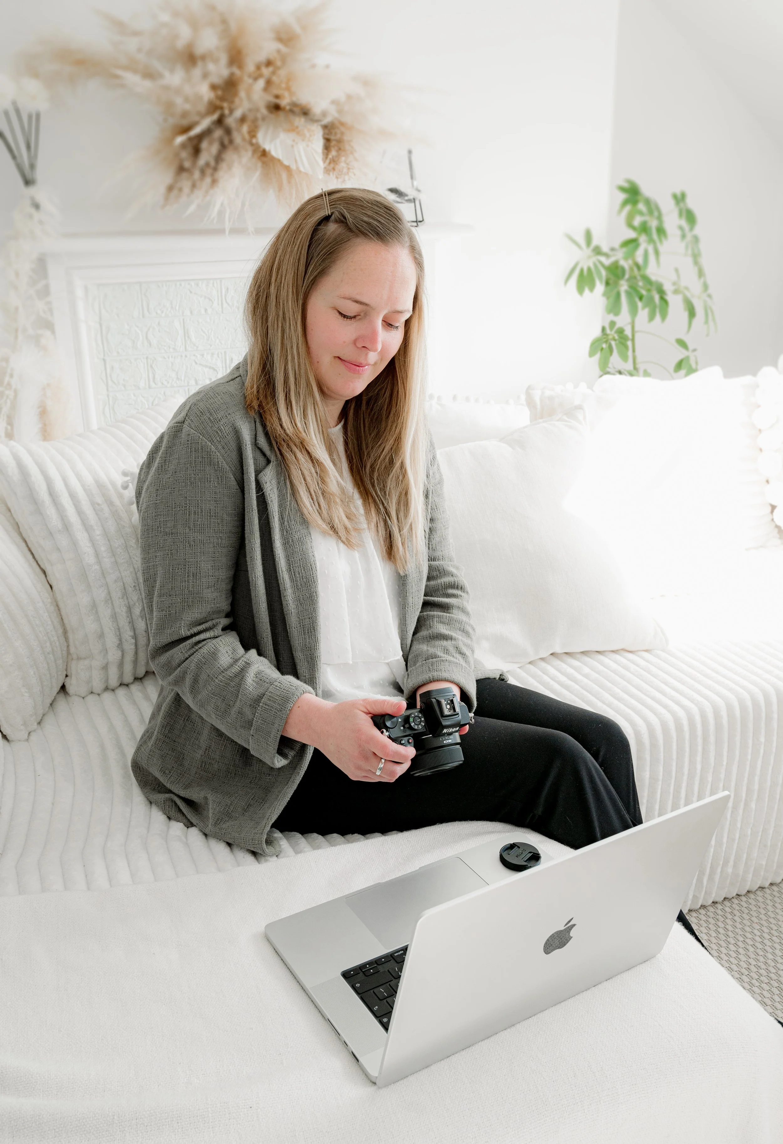 Personal Brand Photographer sat in her studio in Exeter on a white sofa looking at the back of her camera.