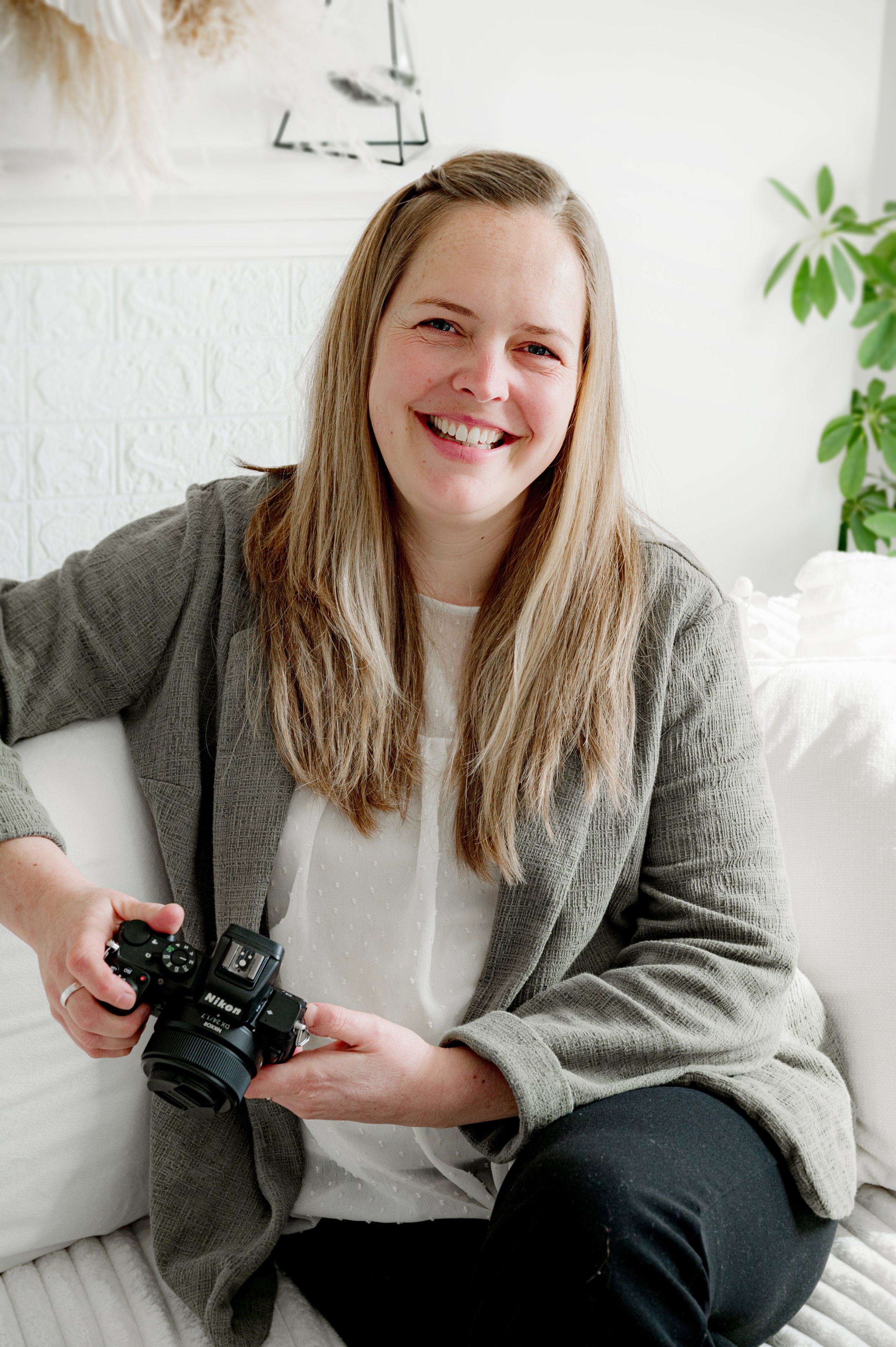 Brand Photographer looking at the camera smiling for her headshot. She is wearing a green top and white blouse in her business portrait