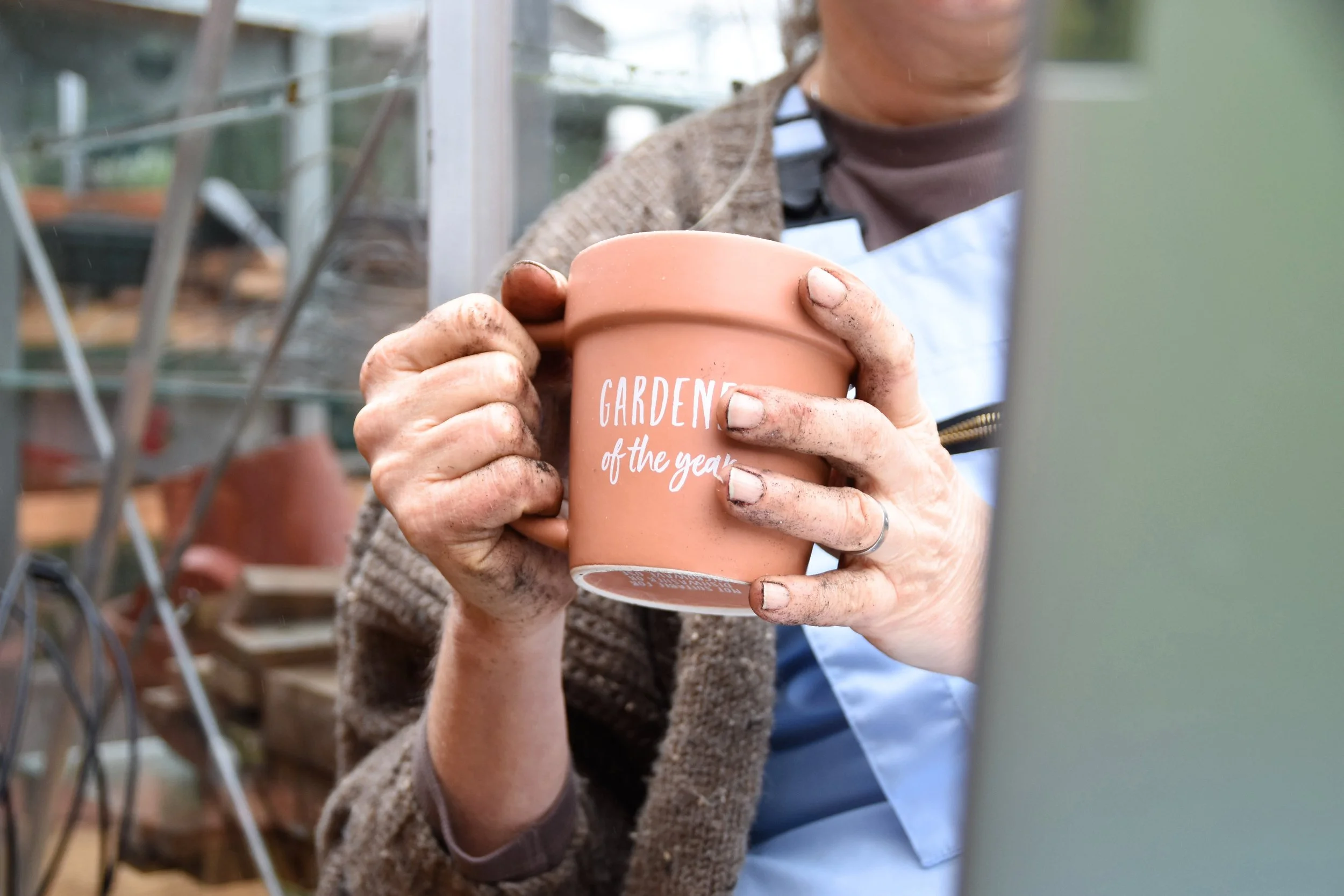 Close up of gardner at work on her laptop holding her pot plant tea cup with soil in her finger tips