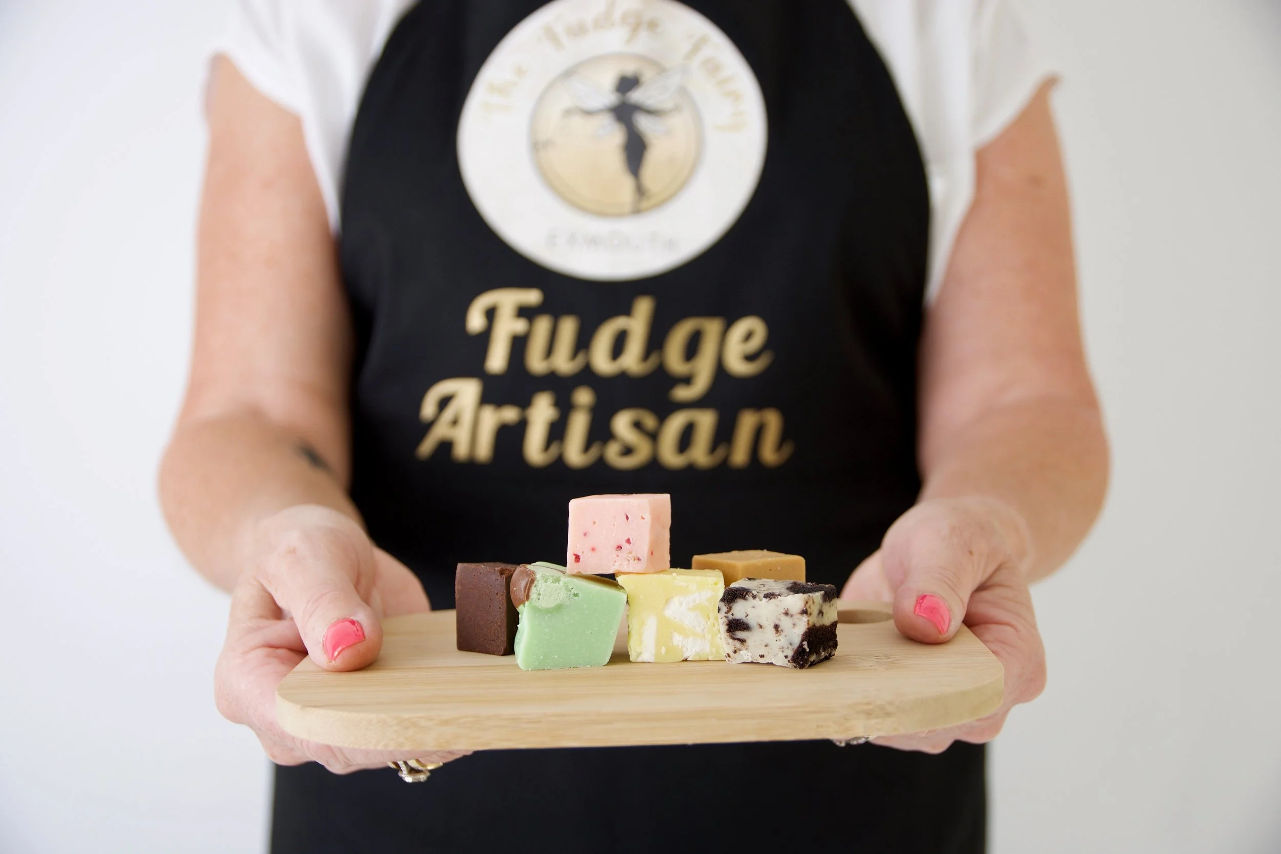 a variety of fudge and flavours being held by the baker on a small chopping board