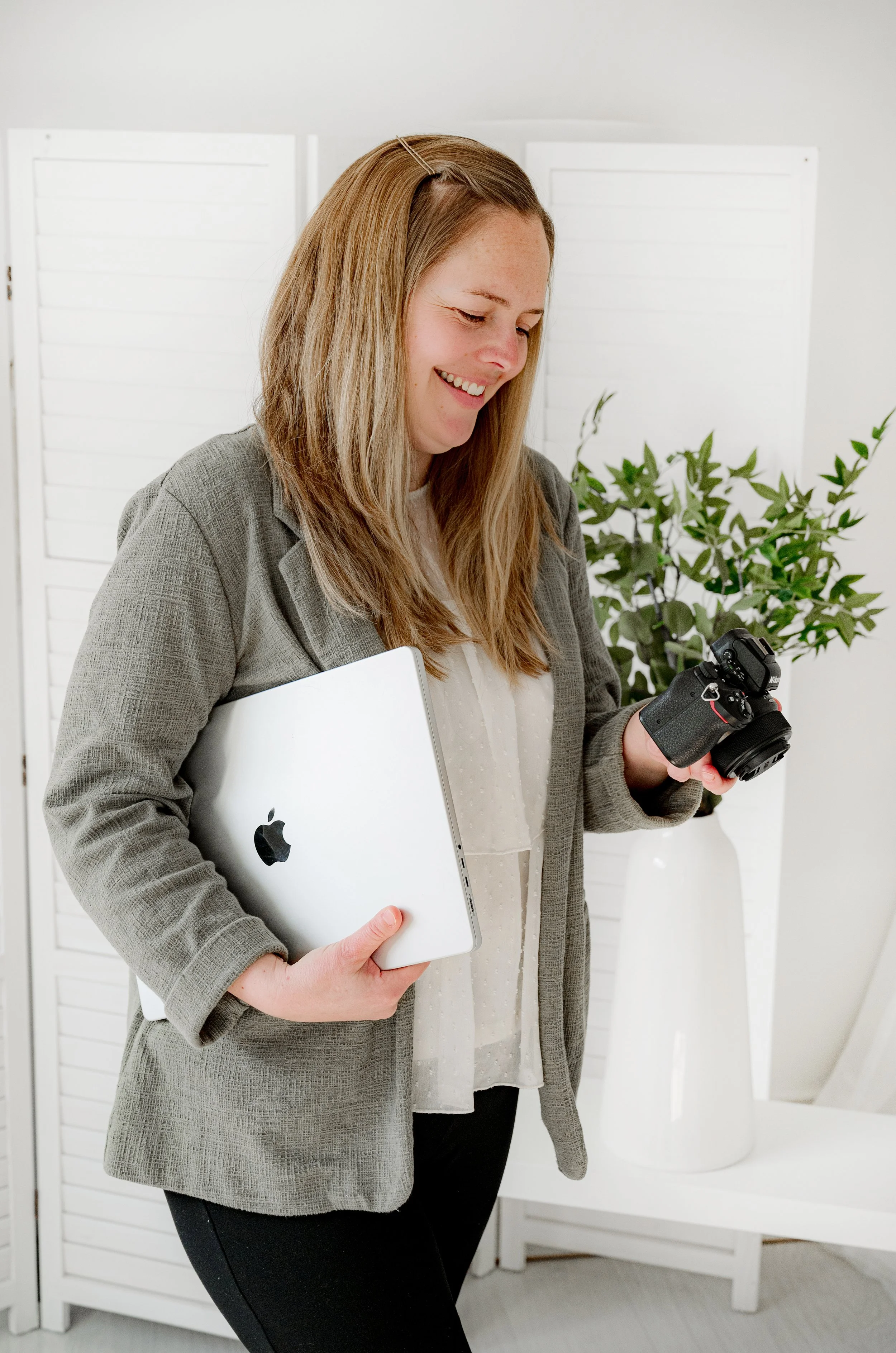Brand photographer looking down at her camera whilst holding her laptop under her arm