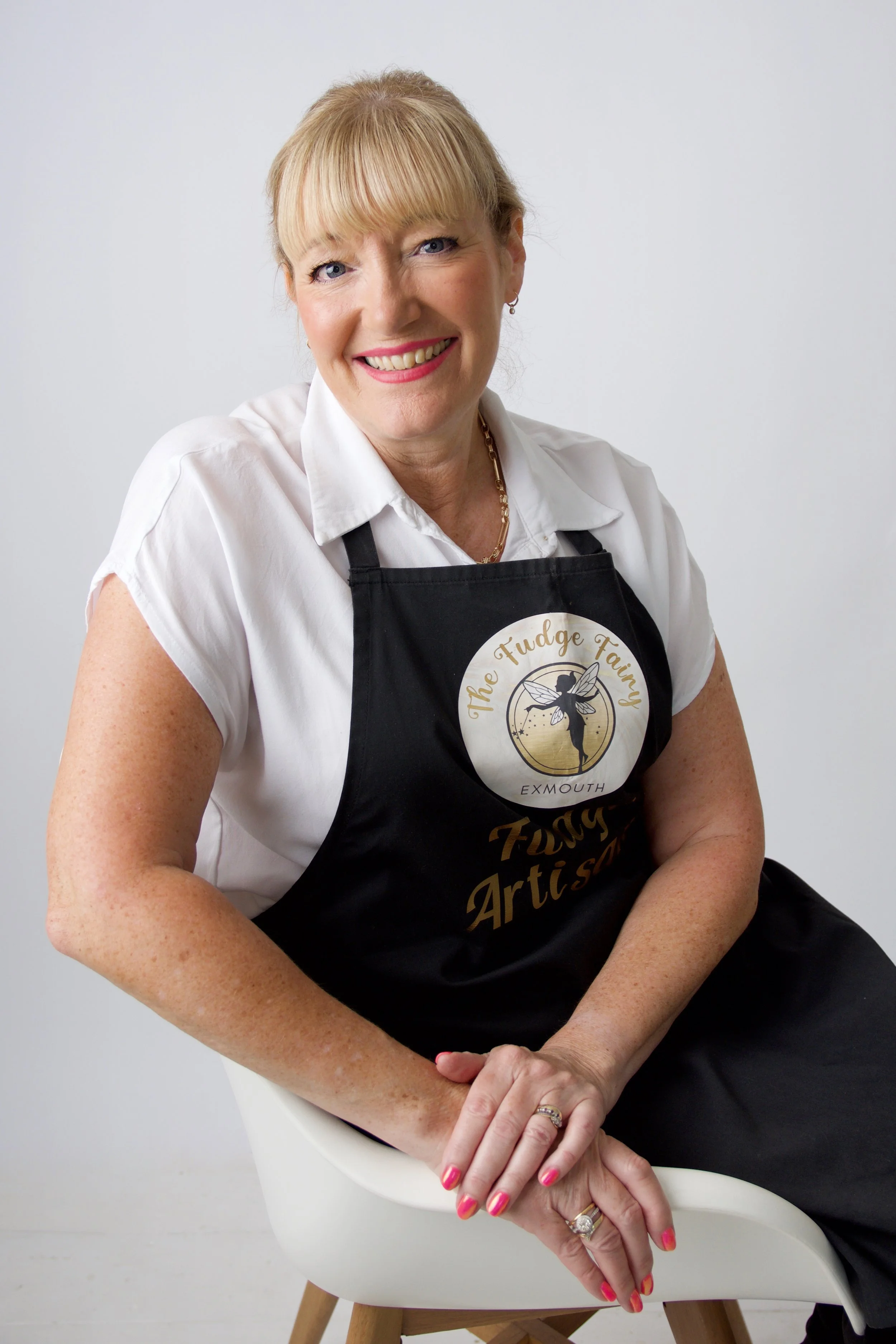 A female baker sat down on a chair wearing her apron and smiling at the camera