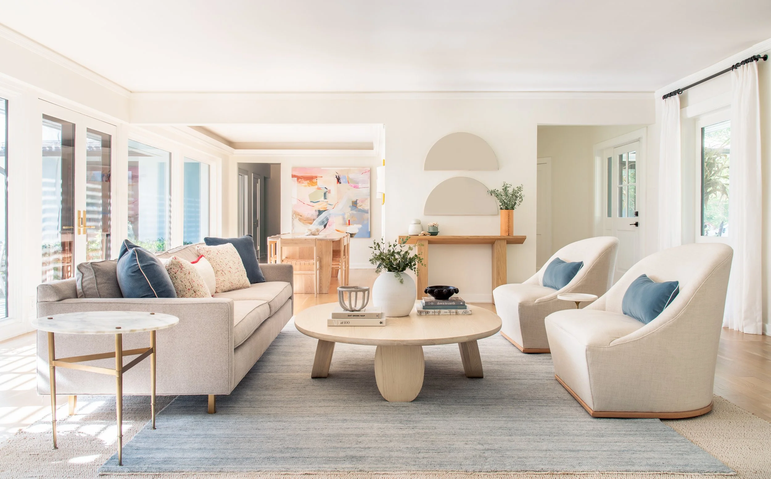 Bright living room with gray couch, round wooden coffee table with plants, and lounge chairs.