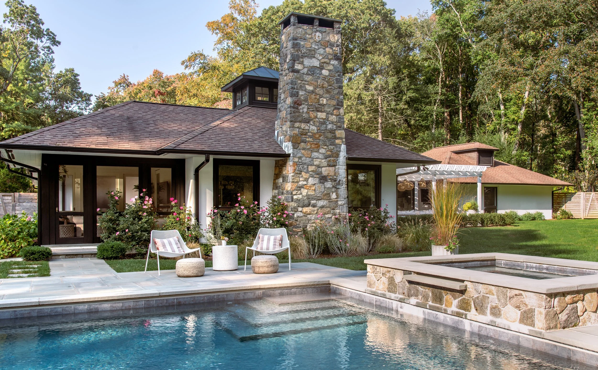 Backyard of house with pool and seating area surrounded by greenery.