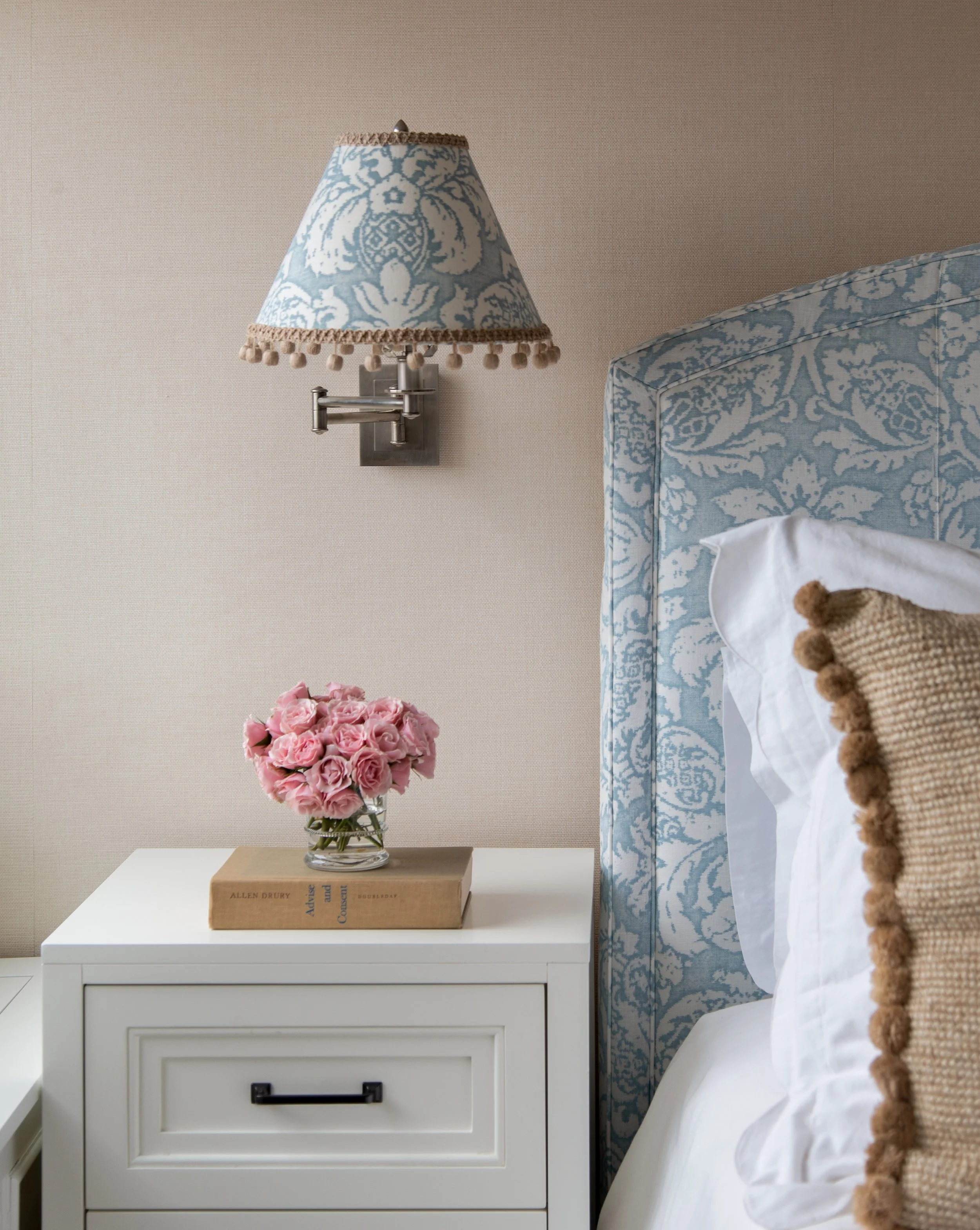 Bed with blue and white bed frame, white bedside table, and mounted lamp with blue pattern.