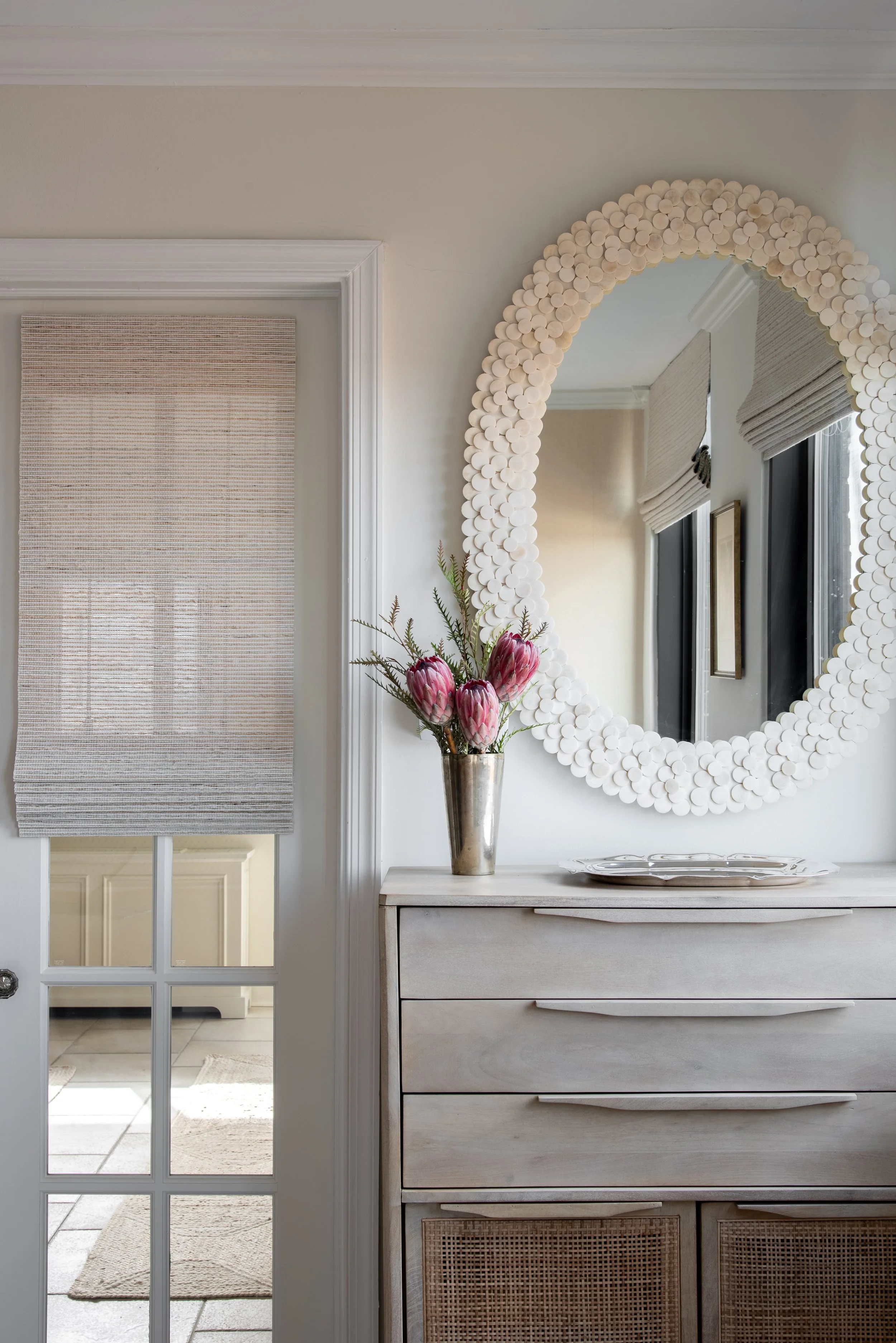 Wooden drawers with flower vase and oval mirror above it.
