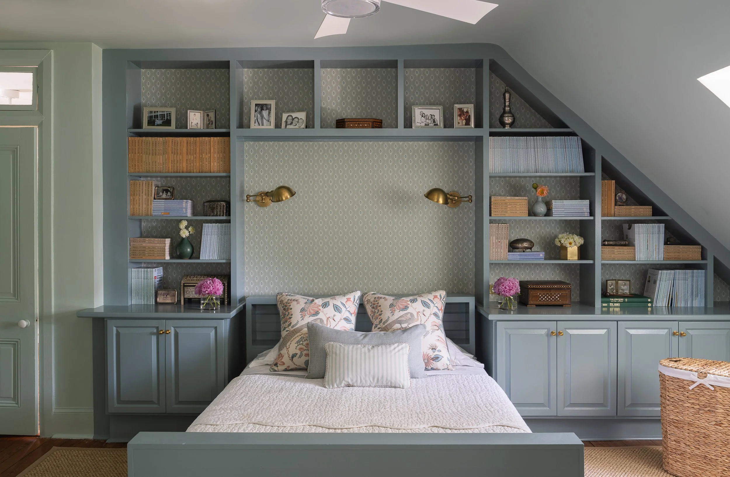 Bedroom with built-in teal shelves and mounted brass reading lights.