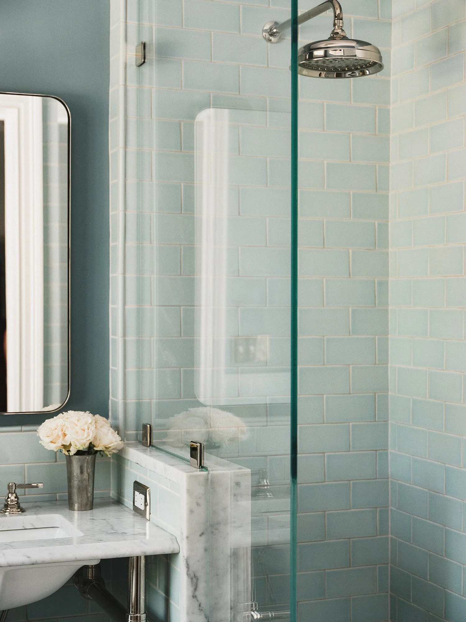 Walk-in shower with mint-colored tiles, a rain shower head, and glass divider.