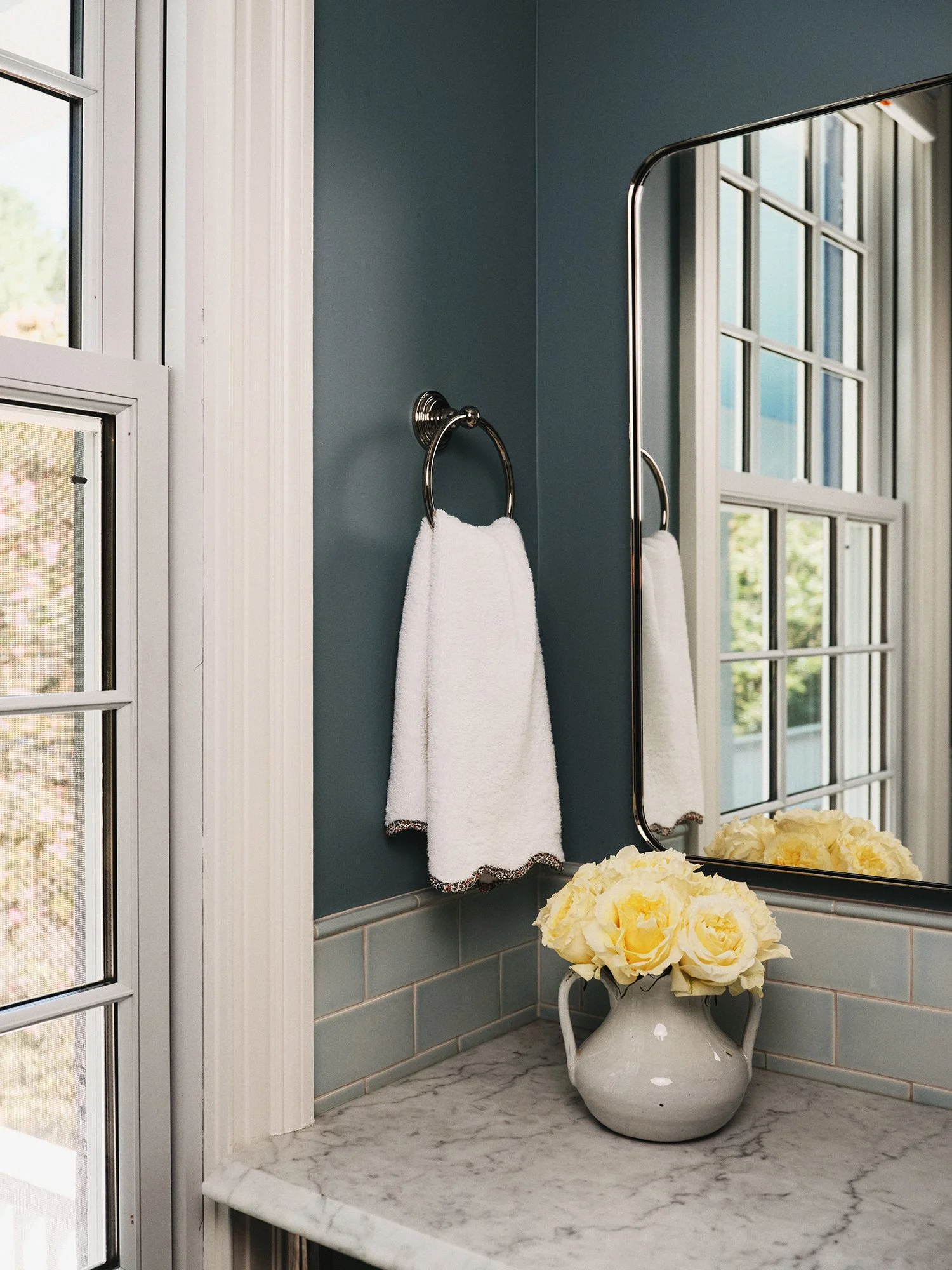 Restroom with turquoise wall, rectangular mirror, yellow flowers, and towel hanger.