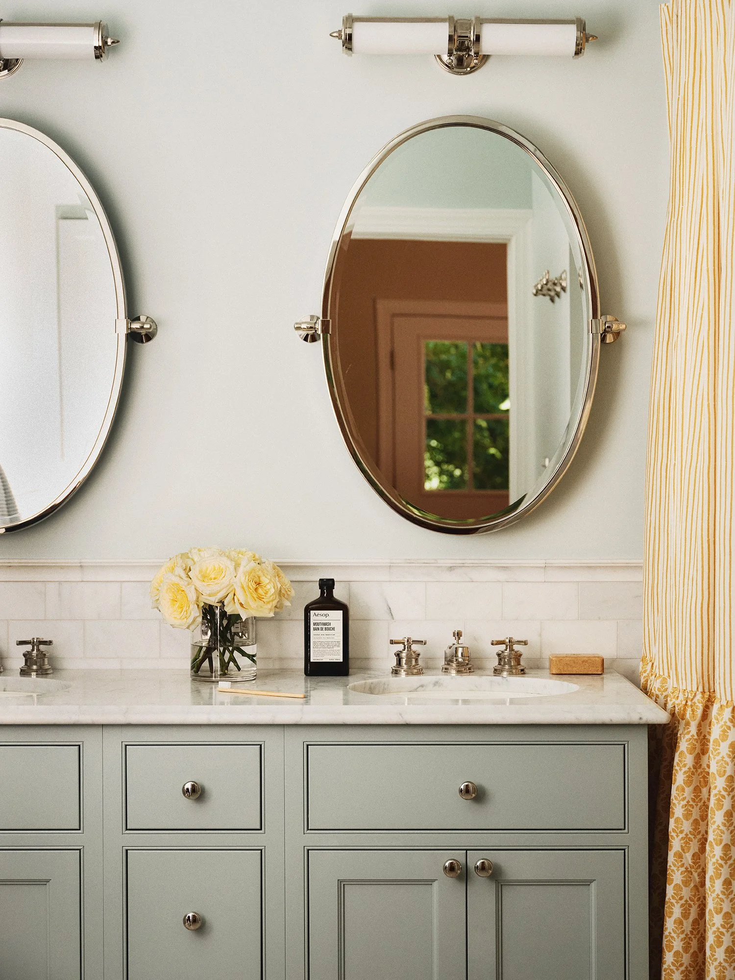 Restroom sink with mint-colored cabinets and oval mirror.