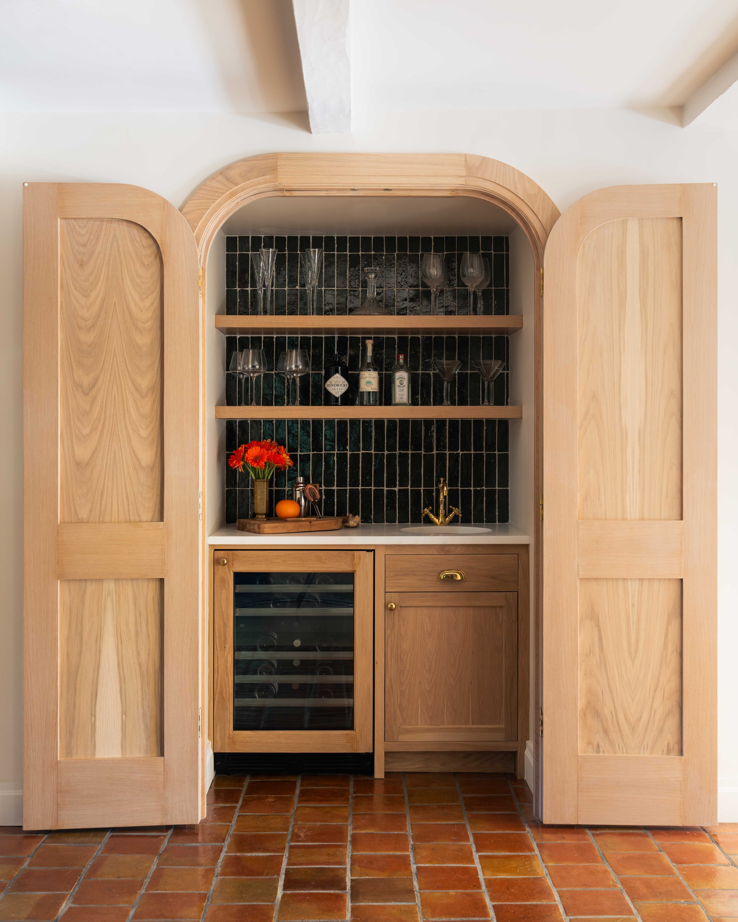 Arched wood beverage cabinet with glassware shelves and a built-in wine fridge.
