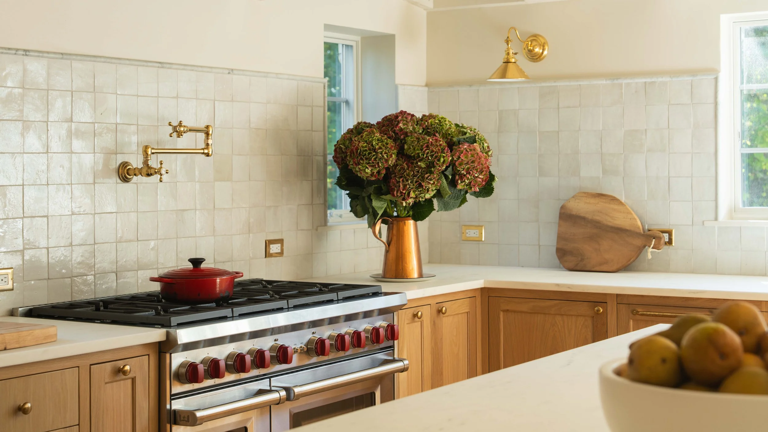 A warm, brightly lit kitchen with off-white tile walls, light wood cabinets, and smooth white countertops.