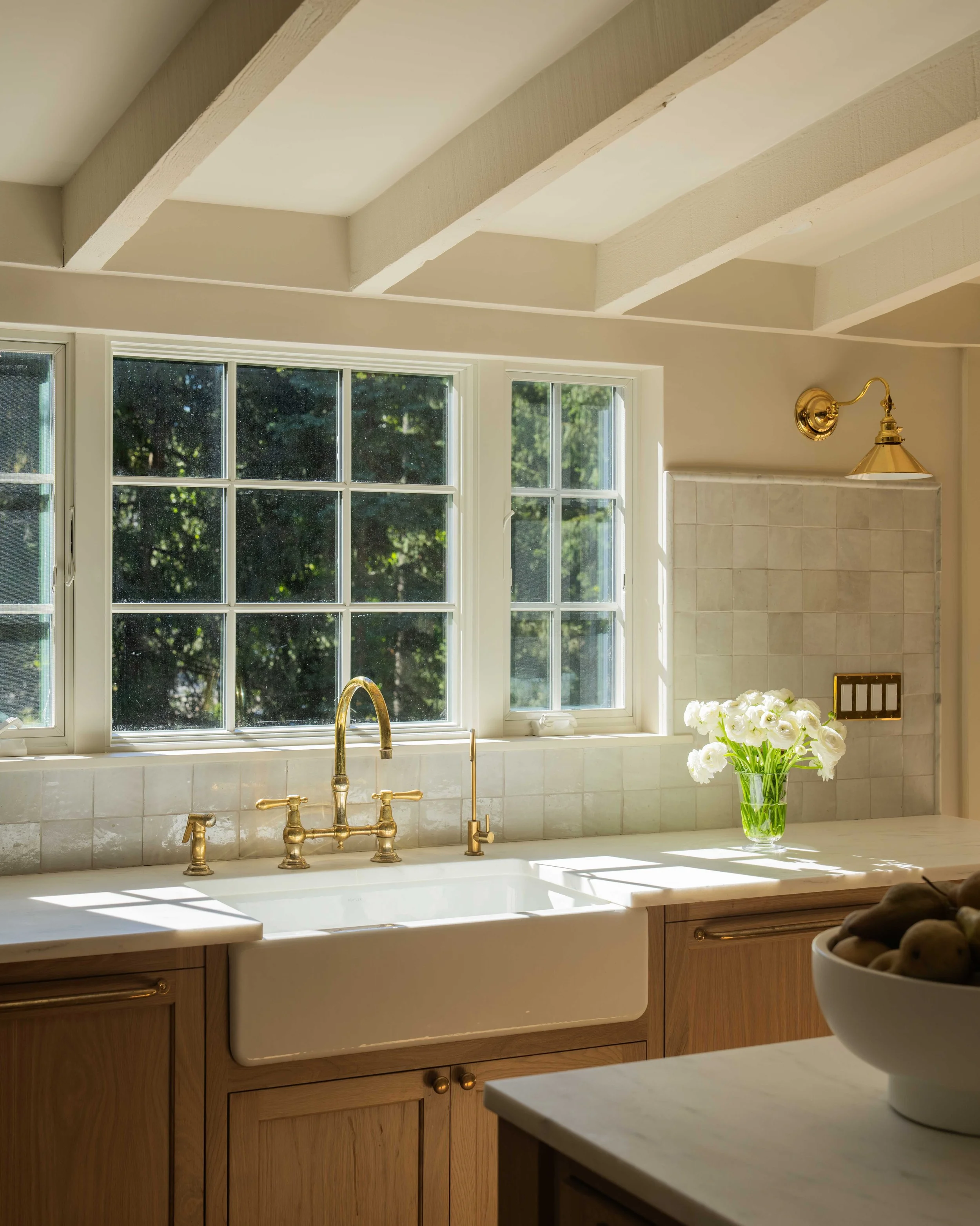 Bright kitchen with a sink, large windows, wood cabinets, and exposed beams.