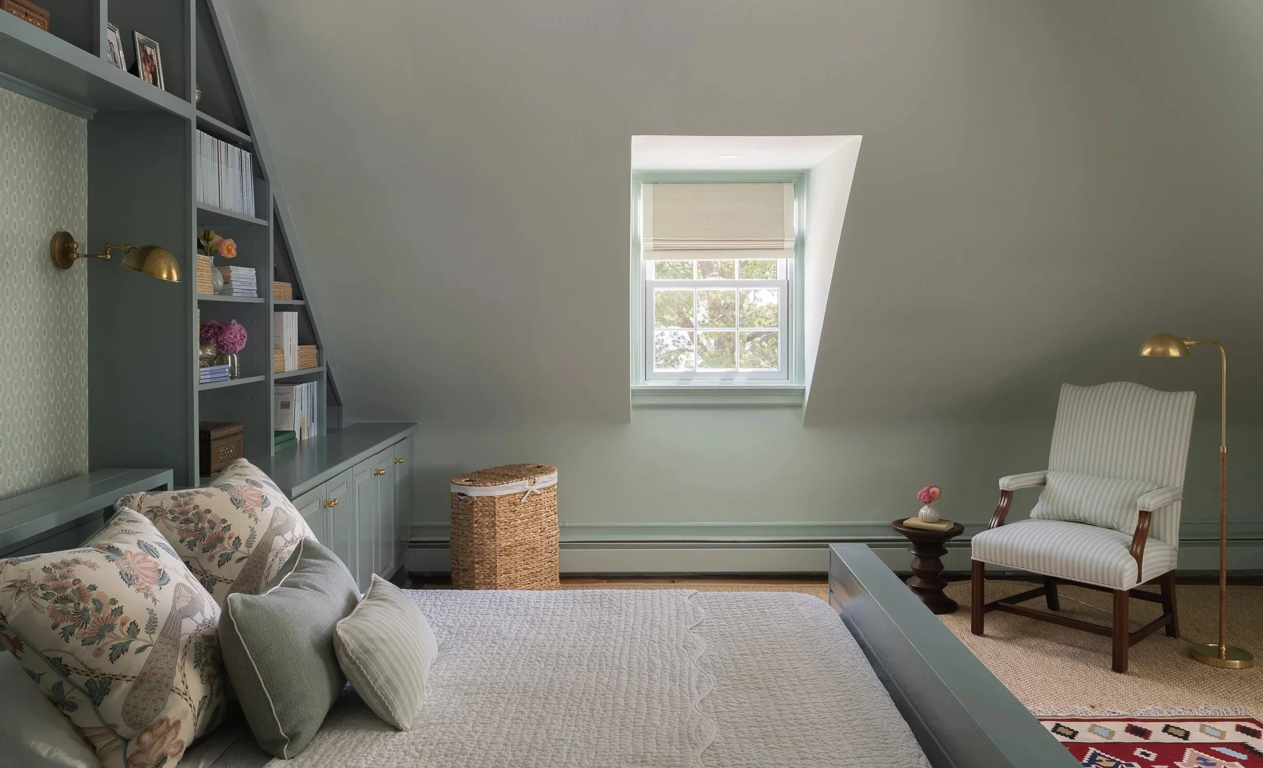 Bedroom with teal built-in shelves, bed, white chair, and sloped ceilings.
