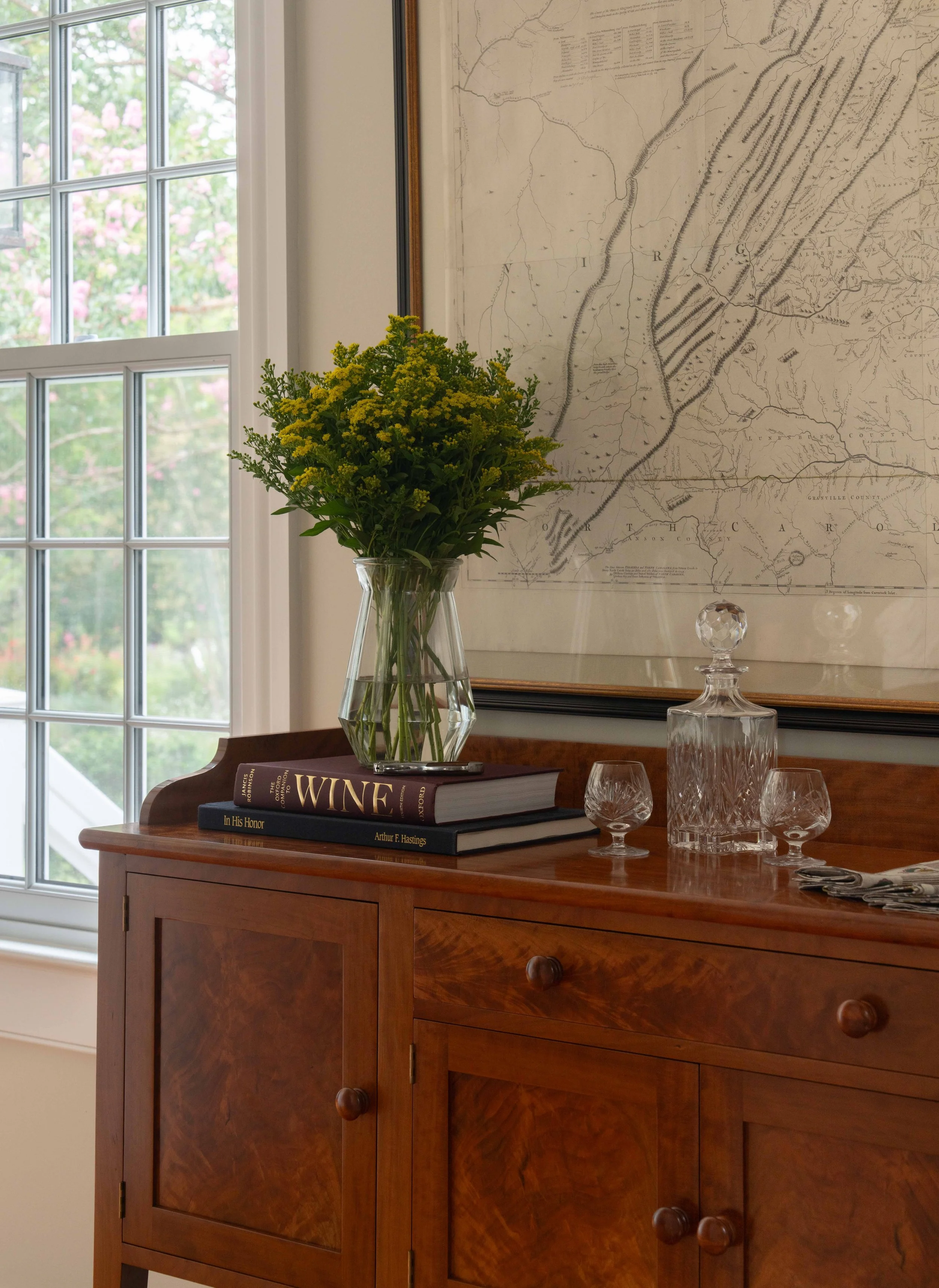 Wooden console table with decorative books, plant vase, drinking glasses.