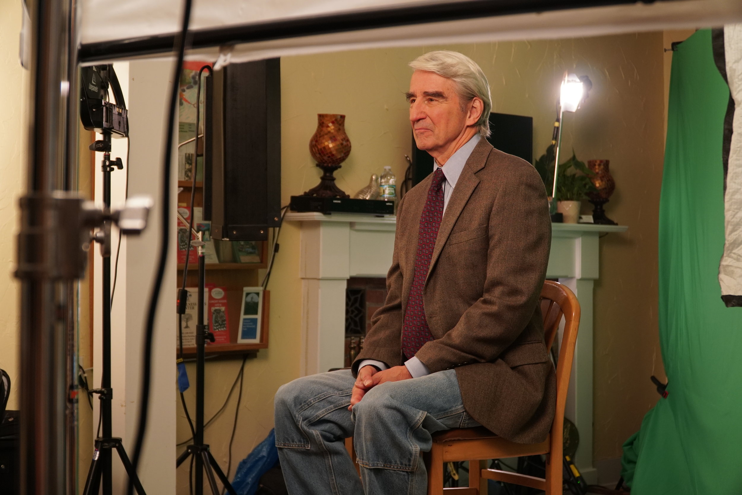  Sam Waterston looking off into the distance with lights in front of him and a green screen behind him 