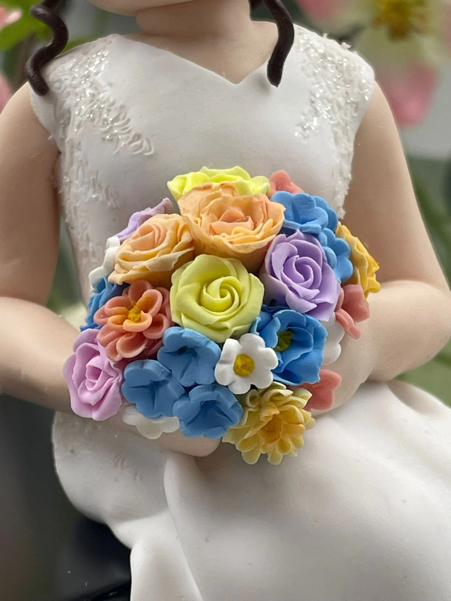 A close up of a polymer clay wedding cake topper of a bride's pastel coloured bouquet