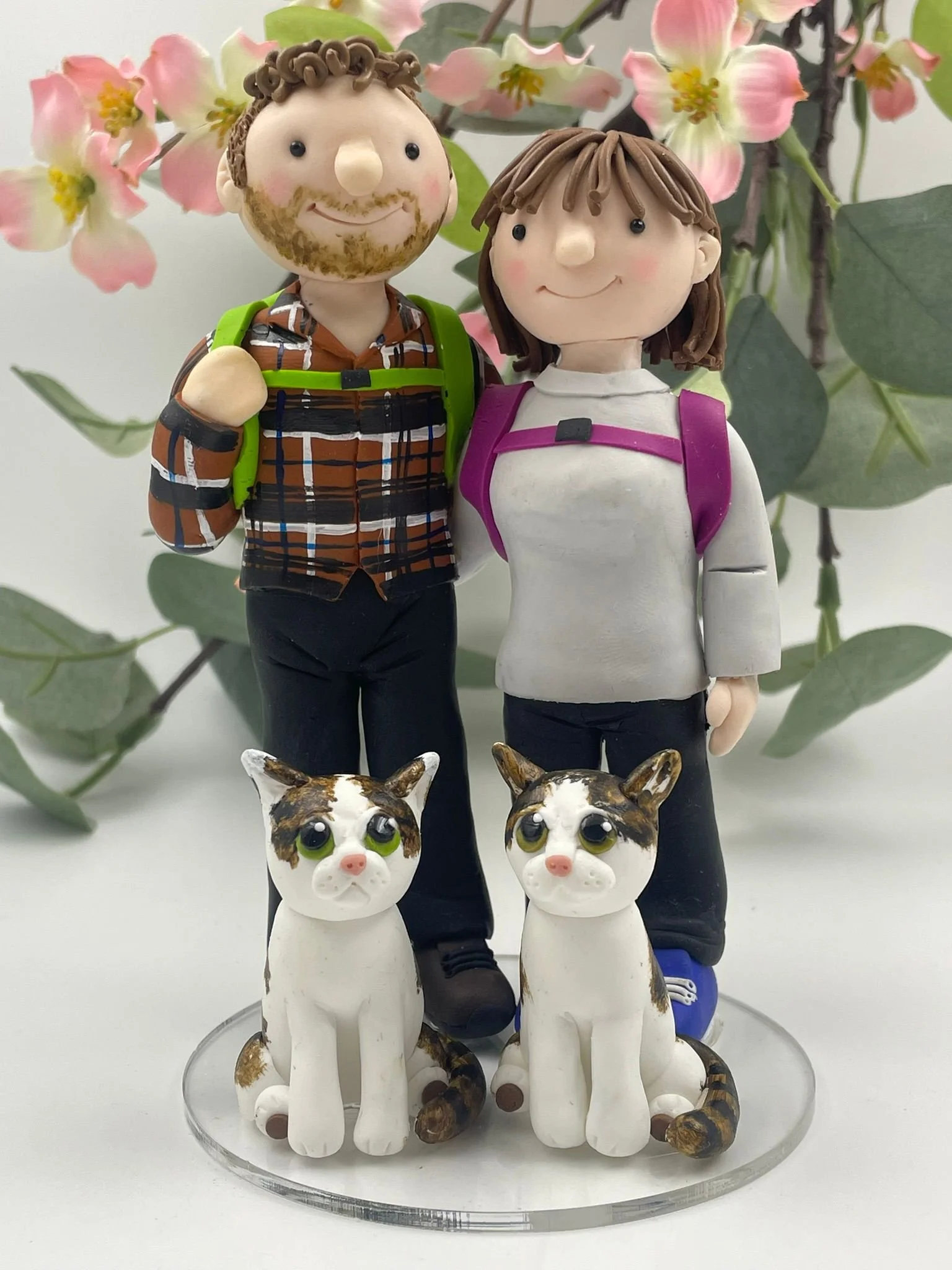 A polymer clay wedding cake topper of a couple in hiking gear with two cats