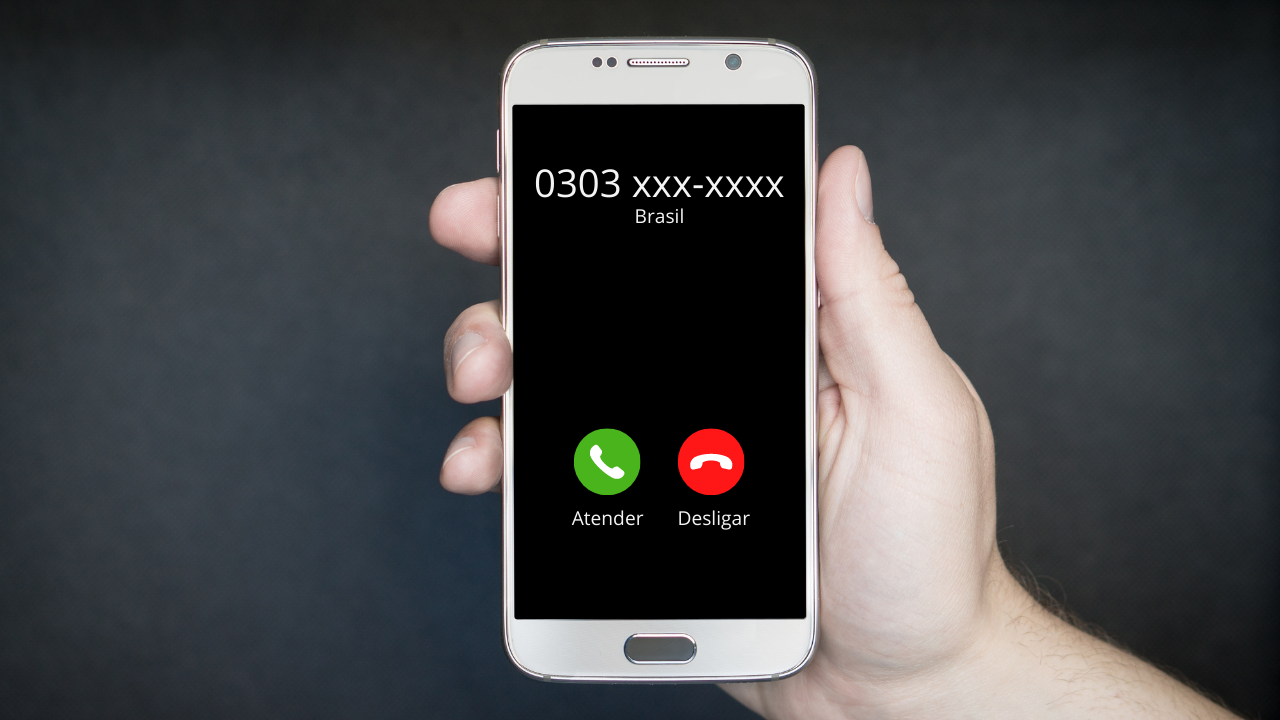 Mão segurando um smartphone com um número que tem o prefixo 0303 na tela.