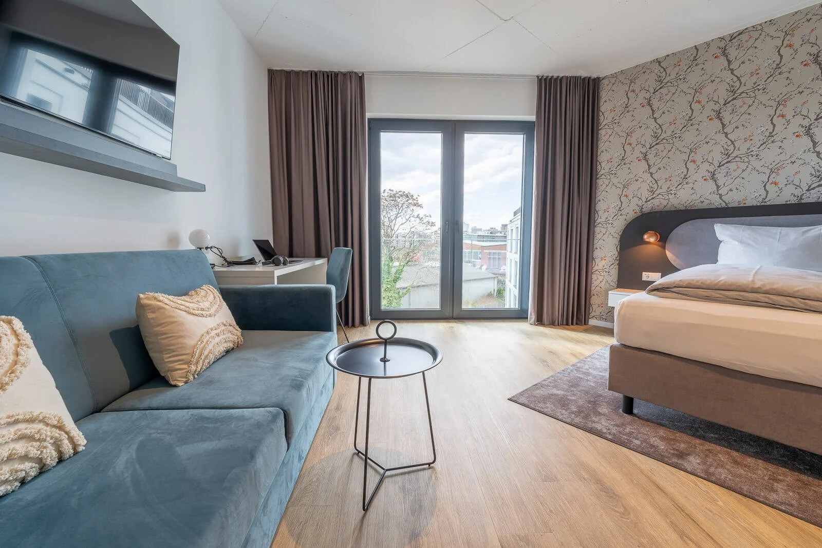 Hotelzimmer mit blauem Sofa, Schreibtisch und Balkonblick – gemütliches und modernes Design.