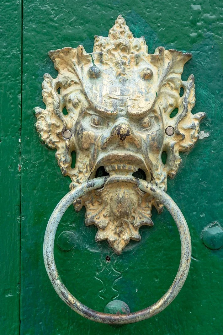  Detailaufnahme eines kolonialzeitlichen Türklopfers in Form eines grotesken Gesichts an einer grünen Holztür in Mompox. 
