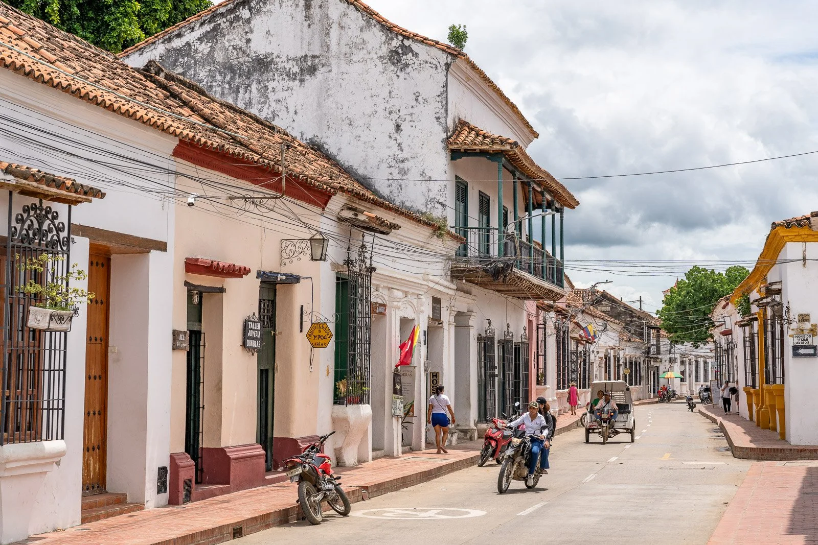  Koloniale Straßenszene in Santa Cruz de Mompox mit Motorrädern, Fußgängern und bunt gestrichenen Häusern im karibischen Stil. 