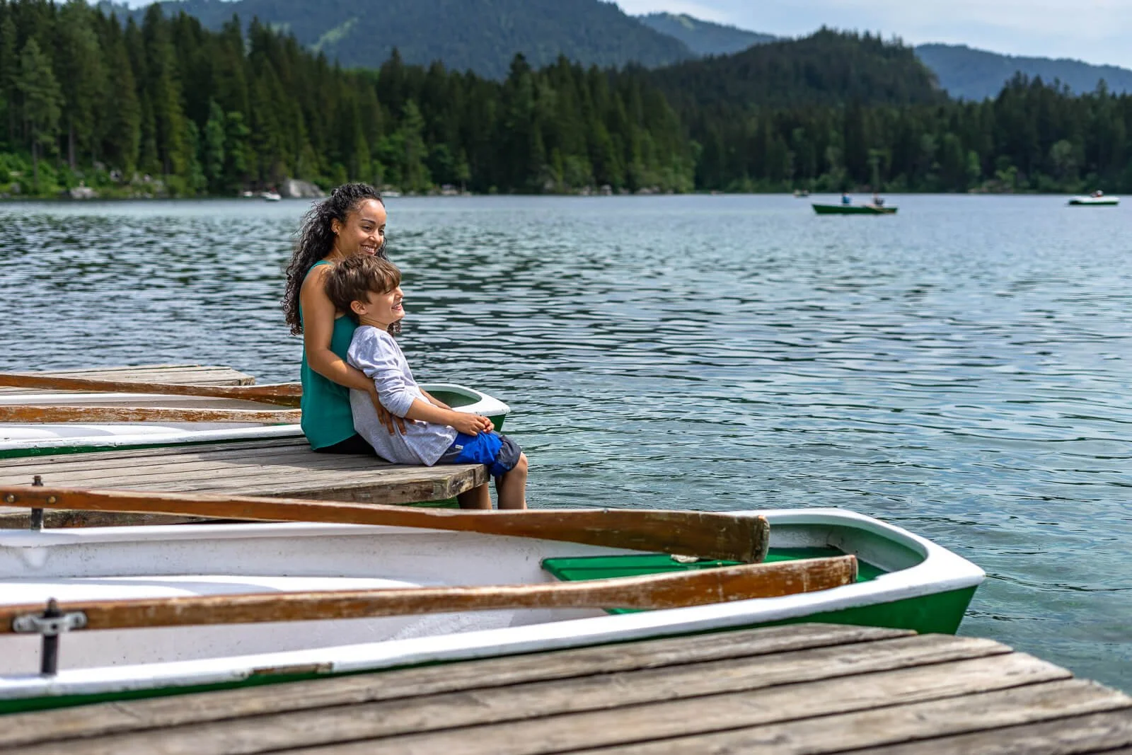  Familie sitzt am Steg am Hintersee bei Ramsau im Berchtesgadener Land, Ruderboote liegen am Ufer 