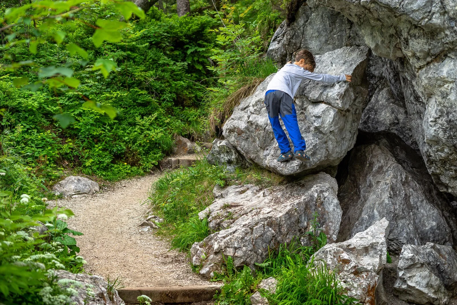  Kind klettert auf Felsen im Zauberwald bei Ramsau im Berchtesgadener Land, naturbelassener Wanderpfad 