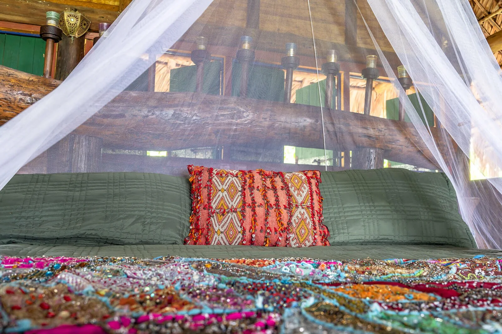 Detailaufnahme eines Boutique-Hotelbetts mit buntem Deko-Kissen und Moskitonetz in einer Eco-Lodge.