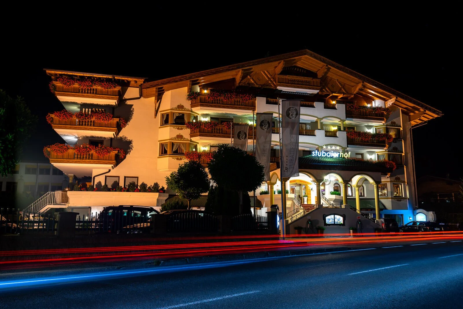 Nachtaufnahme des beleuchteten Hotels Stubaierhof im Stubaital mit Lichtspuren vorbeifahrender Autos.