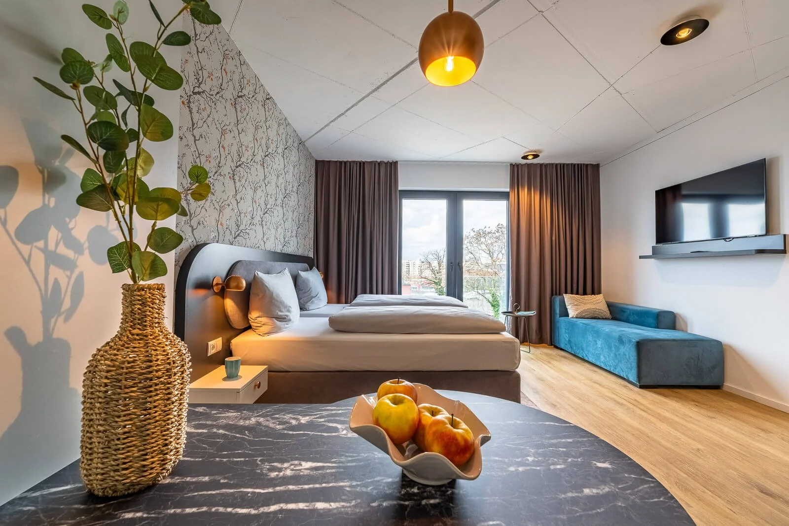 Hotelzimmer mit Blumenarrangement, großem Doppelbett und bodentiefen Fenstern – hochwertige Hotelfotografie in Frankfurt.