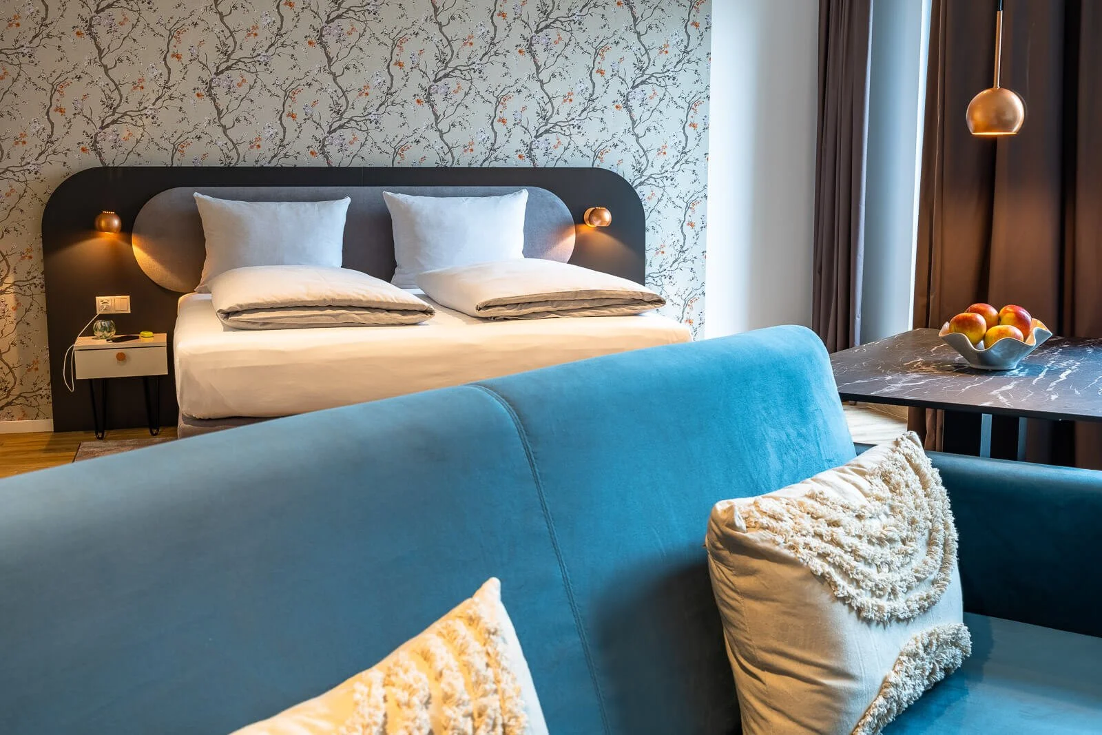 Helles Hotelzimmer mit elegantem Bett, blauem Samtsofa und dekorativer Apfelschale – stilvolle Zimmeraufnahme.